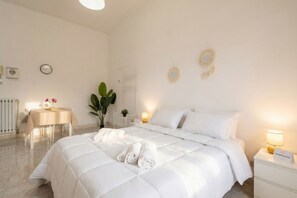 A hotel room with a large bed, bedside tables, a small table with chairs, a potted plant, and wall decorations.