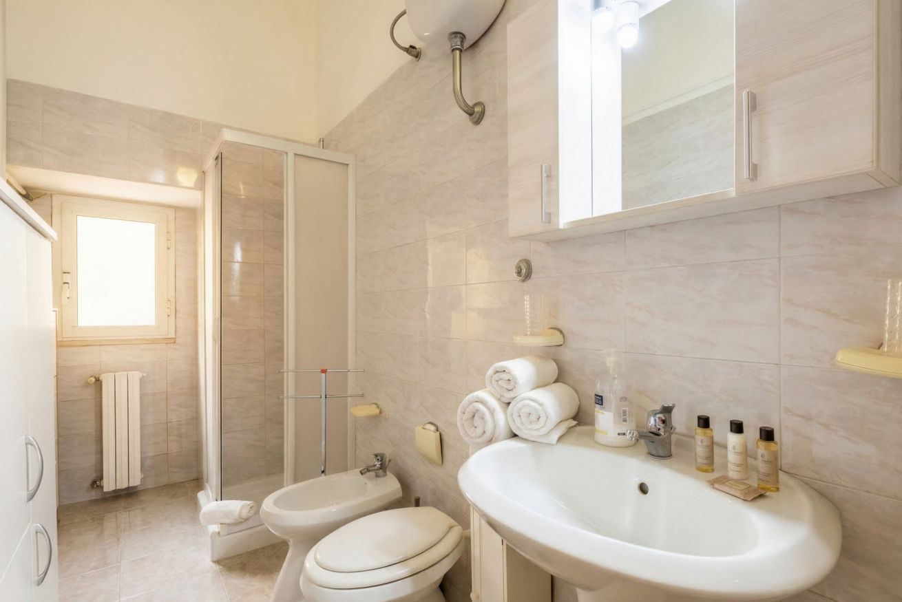 Une salle de bain avec une douche, deux toilettes, un lavabo et un miroir.