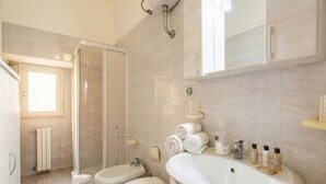 A bathroom with a shower, two toilets, a sink, and a mirror.