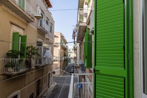 A narrow street with buildings on both sides, some with balconies and shutters.