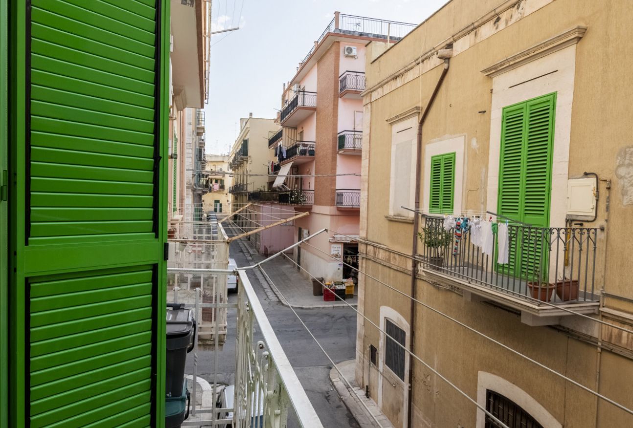 Una calle estrecha flanqueada por edificios, con balcones y celosías verdes.