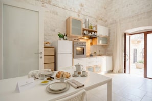 Une cuisine moderne avec des meubles blancs, un four encastré et un coin repas où la table est mise pour le petit-déjeuner.