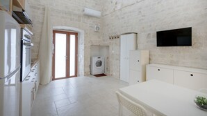 Une cuisine équipée d’un lave-linge, d’un téléviseur fixé au mur et d’un coin repas avec une table et des chaises.