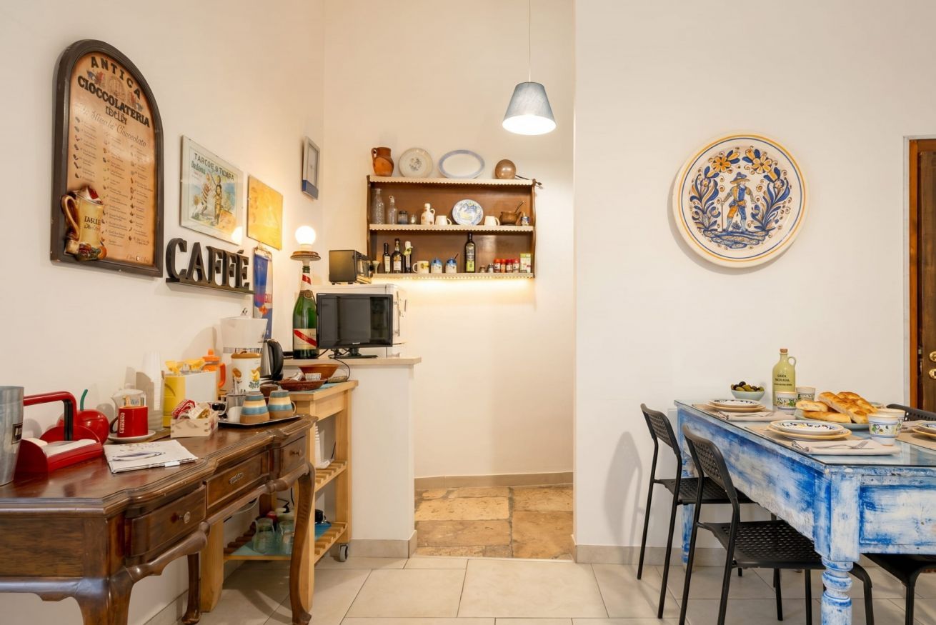A kitchen with a wooden table, a counter with various items, and a wall-mounted shelf with plates and a decorative plate.