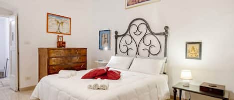 A neatly made bed with white bedding, a wooden dresser, and a bedside table with a lamp.