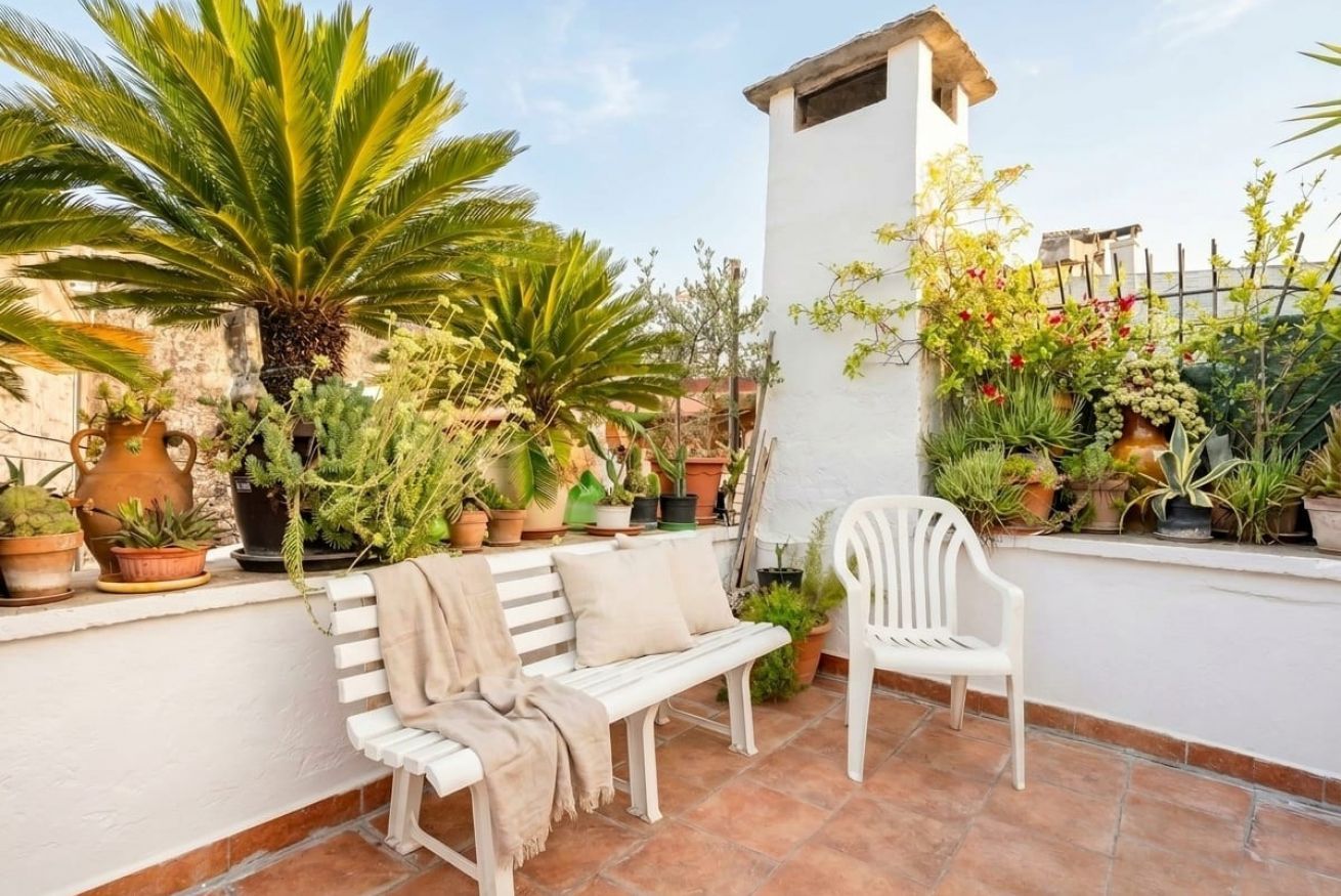 Una terraza con plantas en macetas, un banco blanco y una silla blanca.