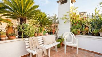 Una terraza con plantas en macetas, un banco blanco y una silla blanca.