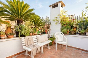 Une terrasse agrémentée de plantes en pot, d’un banc blanc et d’une chaise blanche.