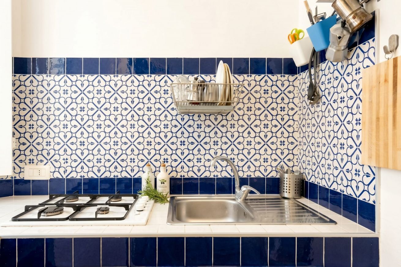 A kitchen with blue and white patterned tiles, a stainless steel sink, and a hanging rack with utensils.