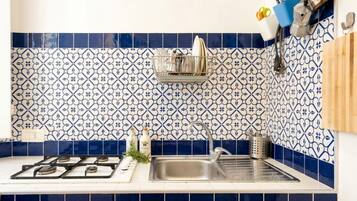 A kitchen with blue and white patterned tiles, a stainless steel sink, and a hanging rack with utensils.