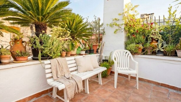 Um terraço com vasos de plantas, um banco branco e uma cadeira branca.