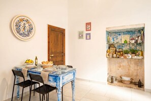 A dining area with a table set for four, a wooden door, and a shelf with various items.