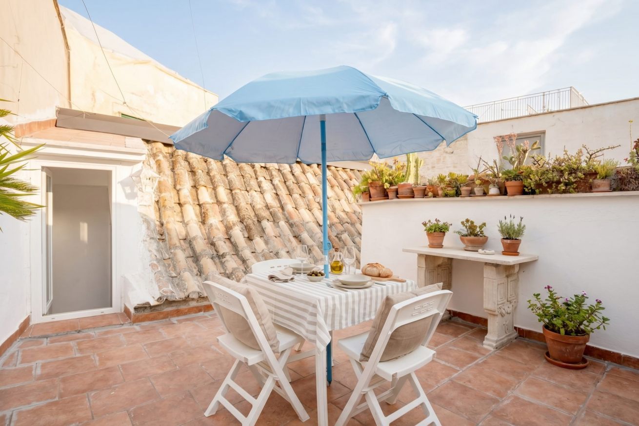 Un patio al aire libre con una mesa, sillas, un paraguas azul y plantas en macetas.