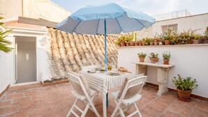 An outdoor patio with a table, chairs, a blue umbrella, and potted plants.