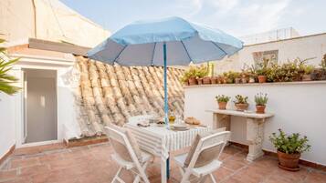 Un patio al aire libre con una mesa, sillas, un paraguas azul y plantas en macetas.