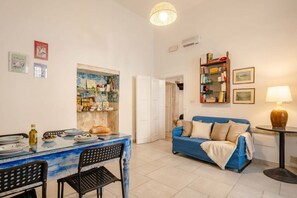 Un salon avec un canapé bleu, une table à manger avec des chaises, une bibliothèque et une lampe.