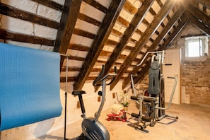 An attic room with a ceiling fan, exercise equipment, and a window.