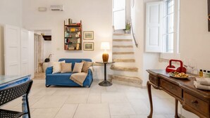 A living room with a blue sofa, a coffee table, a lamp, a bookshelf, and a staircase.