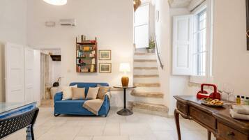 Una sala de estar con un sofá azul, una mesa de centro, una lámpara, una estantería y una escalera.