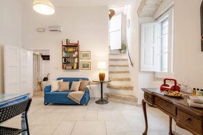 Un salon avec un canapé bleu, une table basse, une lampe, une bibliothèque et un escalier.
