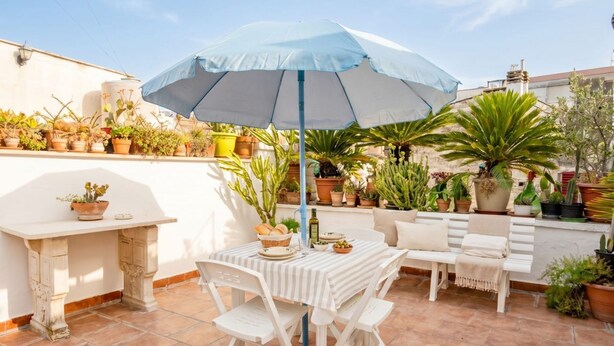 A patio with a table and chairs, an umbrella, and various potted plants.
