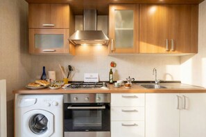 Une cuisine moderne équipée d’un lave-linge, d’un four, d’une cuisinière en acier inoxydable et de meubles en bois.