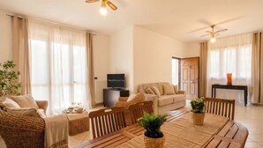 Un'ampia zona giorno con tavolo da pranzo, mobili in vimini, televisore e ventilatore a soffitto.