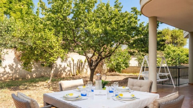 Un'area pranzo all'aperto con mobili in vimini, una tovaglia bianca e un boccale.