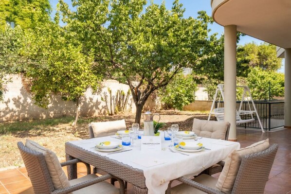 An outdoor dining area with wicker furniture, a white tablecloth, and a pitcher.