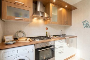 Une cuisine dotée de meubles en bois, d’une hotte en acier inoxydable, d’un four encastré et d’un lave-linge.