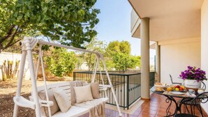 Un patio con un'altalena bianca, un tavolo imbandito per la colazione e vista sugli alberi.