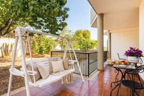 A patio with a white swing, a table with breakfast, and a view of trees.