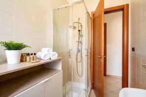 A modern bathroom with a glass-enclosed shower, a wooden vanity, and a potted plant.