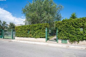 A gated entrance with a hedge, a clear sky, and a tree in the background. - Elisa – 3-Bedroom Beach House with Private Garden (Bari)