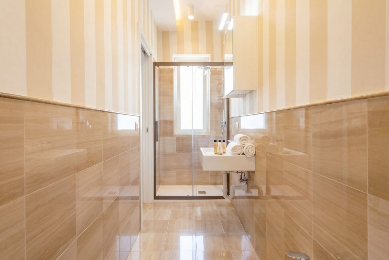 Ein modernes Badezimmer mit Duschkabine aus Glas, einem Waschbecken mit Pflegeprodukten und gestreiften Wänden.