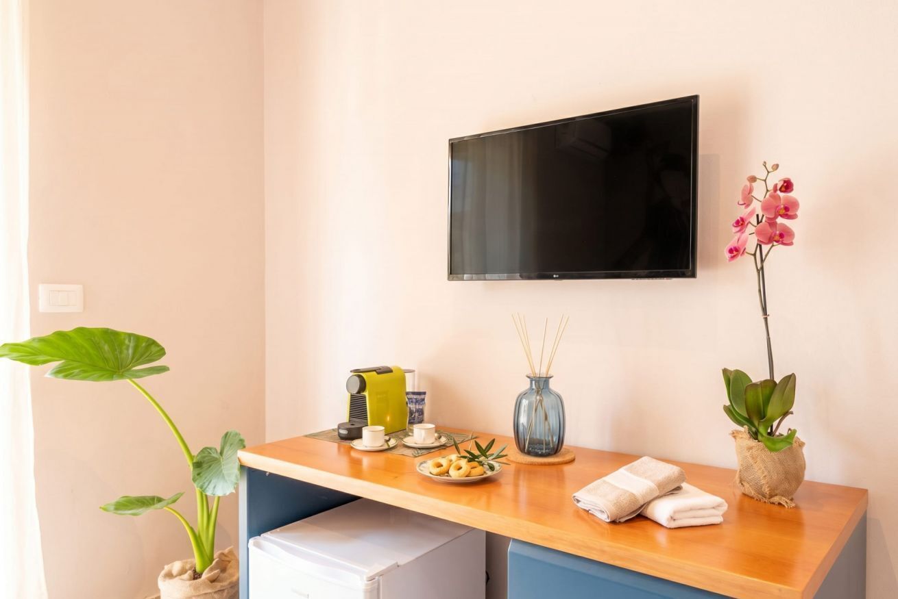 Ein Hotelzimmer mit Schreibtisch aus Holz, einem an der Wand befestigten Fernseher, einer Pflanze und einem Tisch mit Tasse, Untertasse und einem Teller mit Essen.
