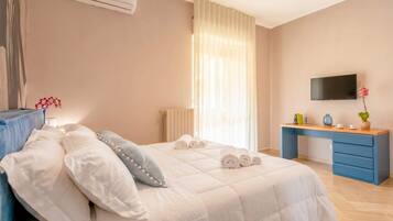 Un dormitorio con cama, escritorio, televisor y ventana con cortinas.