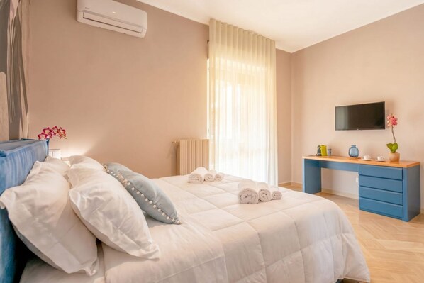 A bedroom with a bed, a desk, a TV, and a window with curtains.