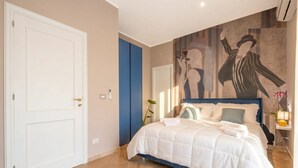 Une chambre à coucher avec un lit, une porte, un mur orné d’une fresque et une table de chevet avec une lampe.