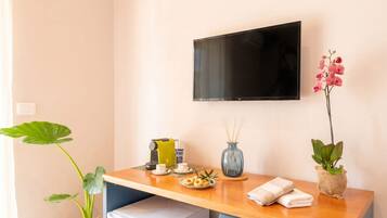 Habitación de hotel con un escritorio de madera, un televisor montado en la pared, una planta y una mesita con una taza, un platillo y un plato de comida.