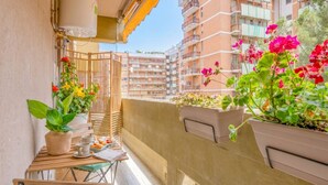 Un balcon agrémenté de plantes en pot, une table avec des tasses et une assiette, et une vue sur des immeubles à plusieurs étages.