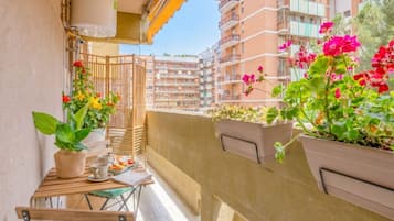 Un balcone con piante in vaso, un tavolo con tazze e un piatto, e vista su edifici a più piani.