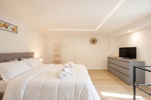 A modern bedroom with a bed, a TV, a dresser, and a wall-mounted shelf.