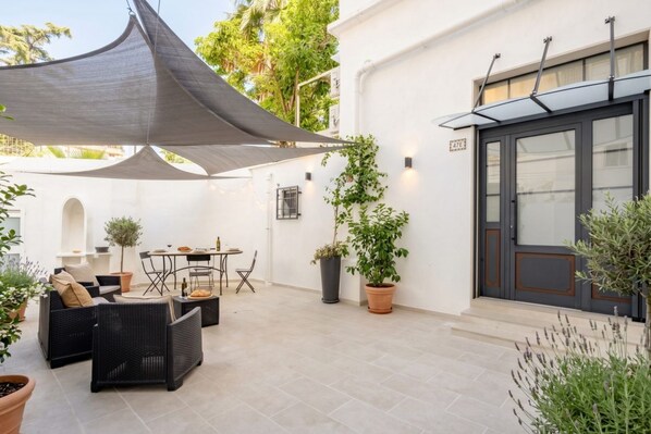 Un espacio al aire libre con patio, una mesa, sillas, plantas en macetas y un paraguas grande.