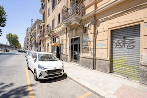 A street with parked cars, a building with a closed shutter, and a sign for a cafe.
