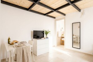 Una habitación moderna y minimalista con comedor, un televisor de pantalla plana, un tocador blanco y un espejo grande.