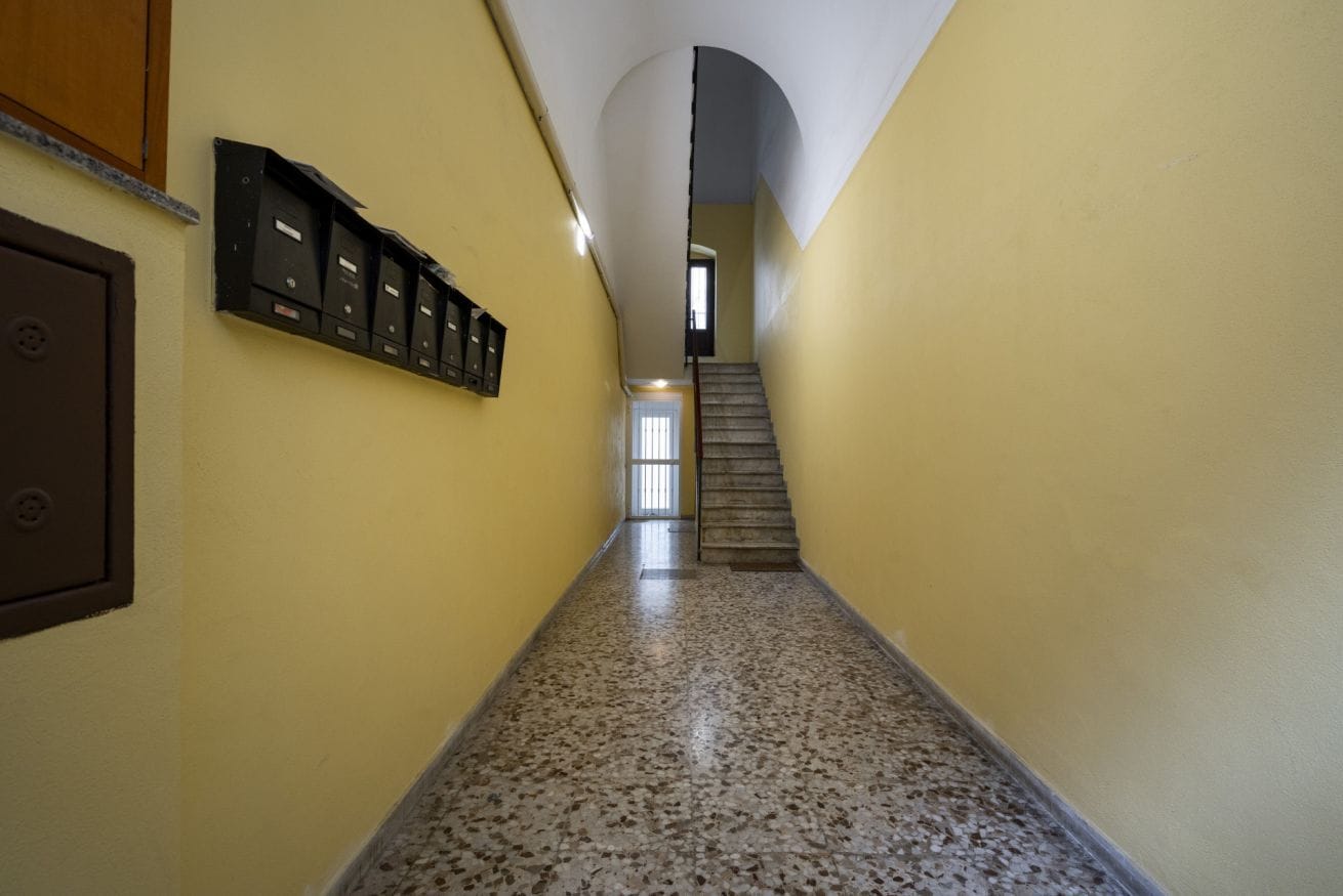 A hallway with a carpeted floor, a staircase, and a row of mailboxes on the wall.