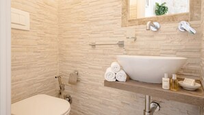 A bathroom with a stone wall, a large vessel sink, a towel rack, and toiletries.