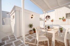 A covered outdoor seating area with a table and chairs, potted plants, and a hanging plant. - Mia & Mimi – Accogliente Rifugio nel Centro Storico (Ostuni)