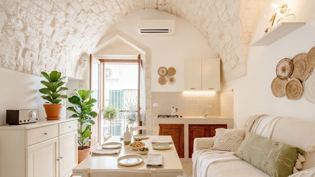A cozy kitchen with a dining area, white cabinets, and a stone wall.